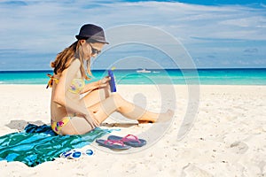 Woman applying sunscreen on her legs before sunbathing. Skin care with protection cream in summer time on the beach