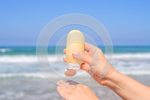 Woman applying sunscreen on skin of hand on a beach of coastline sea. Female relaxation at summer vacation. Back view.