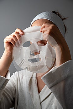 Woman applying textile face mask. Skin care, moisturising, cosmetic procedure.