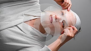 Woman applying textile face mask. Skin care, moisturising, cosmetic procedure. Vertical video