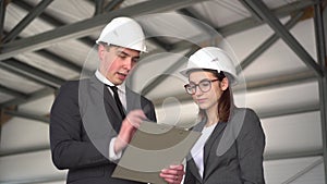 Woman approves the project. Young man and woman in helmets with documents at a construction site. Bosses in suits are