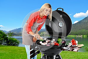 Woman in apron cooking on barbecue grill. Picnic time