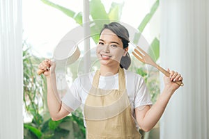 Woman in apron in hand frying pan and kitchen spatula near big window