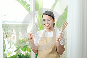 Woman in apron in hand frying pan and kitchen spatula near big window