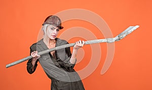 woman architect in protective helmet and boilersuit hold shovel on orange background, engineering