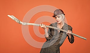 woman architect in protective helmet and boilersuit hold shovel on orange background, engineering
