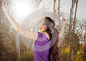 Woman arms in air against blurry trees with flare