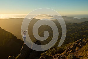 Woman with arms raised stands on mountaintop at sunrise