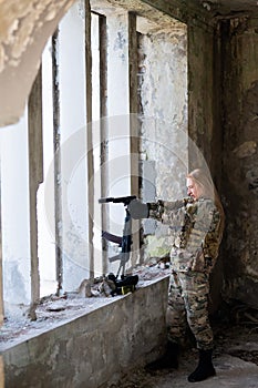 A woman in an army uniform aims to shoot a firearm in an abandoned building.