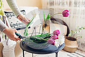 Woman arranges bouquet of tulips flowers at home. Florist cuts stem with scissors. Interior and decor
