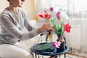 Woman arranges bouquet of tulips flowers at home. Housewife taking care of coziness in apartment. Interior and decor