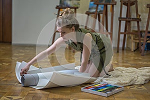 Woman artist in an art studio and unfolds paper rolls