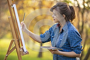 Woman artist drawing a picture on an easel in nature, a girl with a brush and a palette, a concept of creativity and a hobby