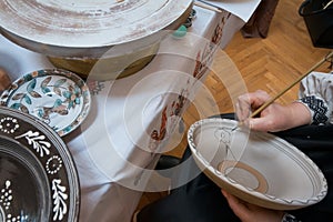 Woman artist handpaint on a handmade clay plate with paint and brush, old traditional Ukrainian painting style
