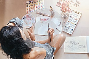 Woman artist painting with brush while sitting on floor at home