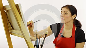 Woman artist painting with paintbrush. The woman draws a picture. The artist on a white background draws on an easel oil