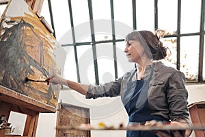 Woman artist paints a picture on canvas. Bright art studio with a large window. Easels and canvases.