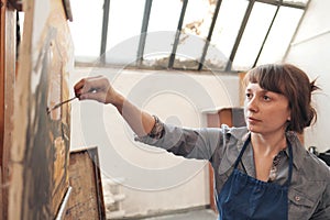 Woman artist paints a picture on canvas. Bright art studio with a large window. Easels and canvases.