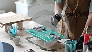 Woman artist pours epoxy resin and smears it with stick on wooden board, using liquid art technique