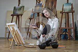 Woman artist sits on the floor in an art studio and paints on canvas