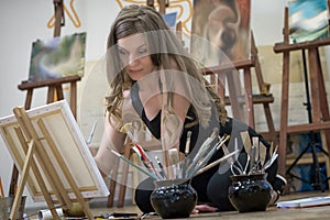 Woman artist sits on the floor in art studio and paints an oil painting.