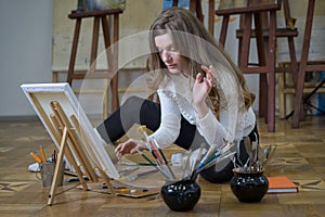 Woman artist sits on the floor in an art studio and paints