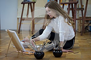 Woman artist sits on the floor in an art studio and paints