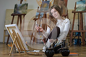 Woman artist sits on the floor in art studio and paints