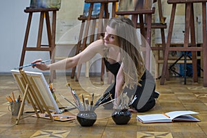 Woman artist sits on the floor in art studio and paints