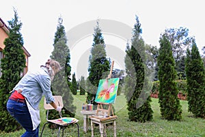 Woman artist stands with brush in hand near easel, looking and f