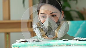 Woman artist wear respirator examines painting after pouring epoxy resin, check quality of work