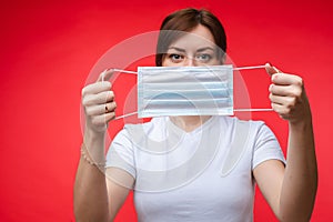 Woman with aseptic mask in hands. Isolate on red.