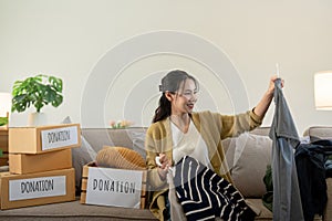 Woman asian holding donation box full with clothes and select clothes. Concept of donation and clothes recycling