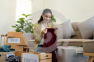 Woman asian holding donation box full with clothes and select clothes. Concept of donation and clothes recycling