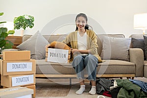 Woman asian holding donation box full with clothes and select clothes. Concept of donation and clothes recycling