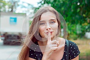 Woman asking for silence or secrecy with finger on lips hush hand gesture city park
