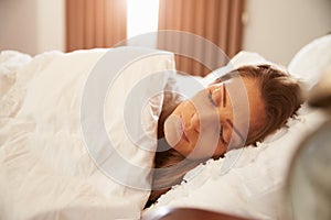 Woman Asleep In Bed As Sunlight Comes Through Curtains