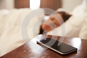 Woman Asleep In Bed With Mobile Phone On Bedside Table