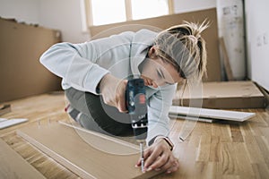 Woman assembling furniture at home with cordless screwdriver