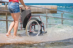 Woman assistant pushing wheelchair at beach with ramp