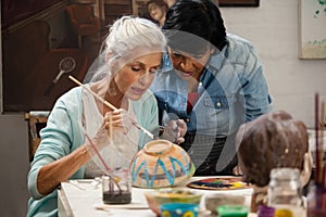 Woman assisting senior woman in painting bowl at drawing class