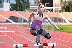 Woman athlete jumping over an obstacle. Running with hurdles. Active lifestyle.