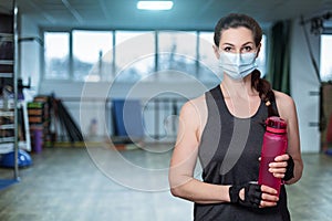 Woman athlete in a mask stands with a bottle of water