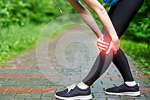 Woman athlete runner touching Knee in pain, fitness woman running in summer park. Healthy lifestyle and sport concept
