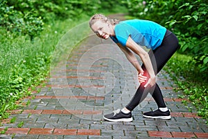 Woman athlete runner touching Knee in pain, fitness woman running in summer park. Healthy lifestyle and sport concept