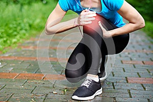 Woman athlete runner touching Knee in pain, fitness woman running in summer park. Healthy lifestyle and sport concept