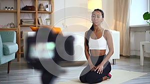 Woman athlete speaking in front of camera and doing exercise in apartment room.