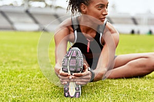 Woman, athlete and stretching legs on grass at stadium in preparation for running, exercise or workout. Active or fit
