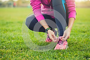 Woman athlete tying shoelaces on sneakers on the green meadow