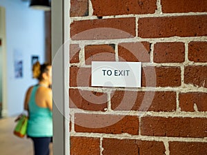 Woman in athletic clothes with in direction of exit sign on brick wall